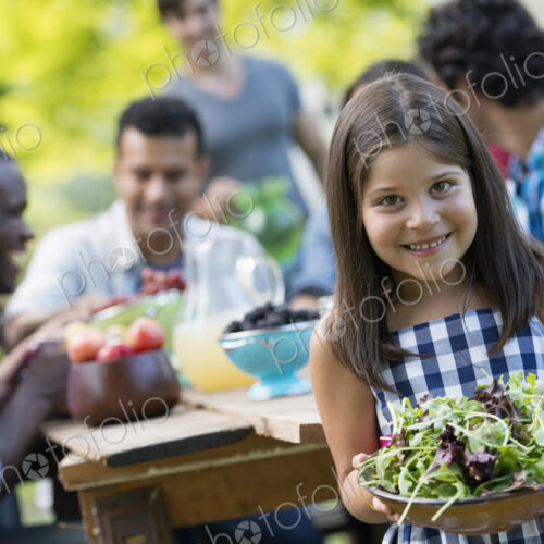 Adults and children around a table in a garden. A child holding a bowl of salad. Adults and children around a table in a garden. A child holding a bowl of salad.