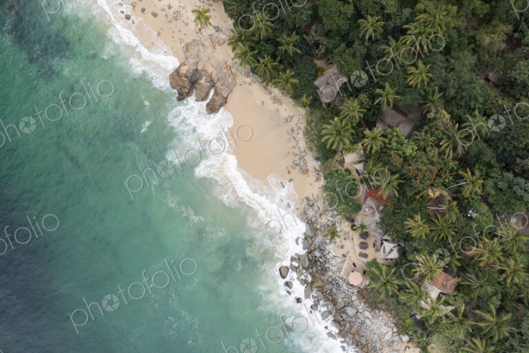 Aerial View of Casitas Marika beach, small beach huts and a thick cover of palm trees…