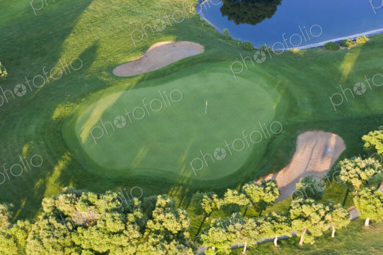 Aerial view of a golf course with lush green lawn, trees and and bunkers.