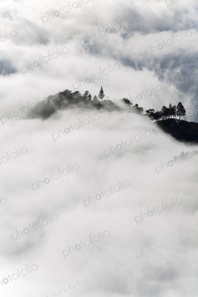 Aerial view of lush mountains on an island, surrounded by clouds.