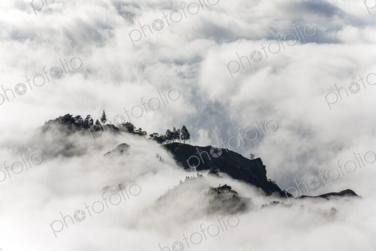 Aerial view of lush mountains on an island, surrounded by clouds.