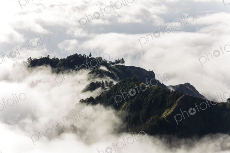 Aerial view of lush mountains on an island, surrounded by clouds.