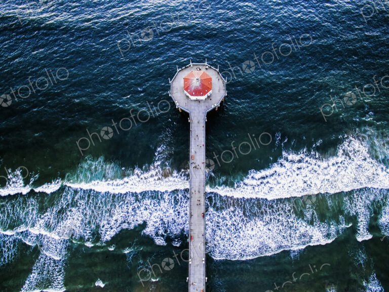 Aerial view of the Manhattan Beach Pier and waves breaking on the shore.