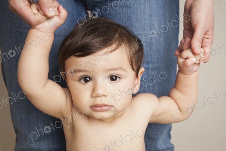 An 8 month old baby boy holding his parent's hands and balancing upright.