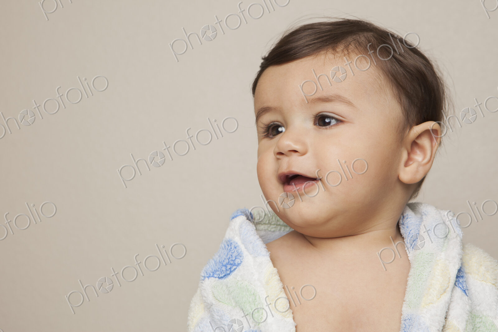 An 8 month old baby boy with a bath towel wrapped around him.