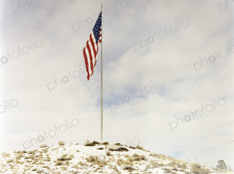 An American flag Stars and Stripes, flying from a flagpole on a small hillock.