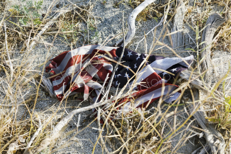 An American flag, crumpled up on the sandy ground, damaged,