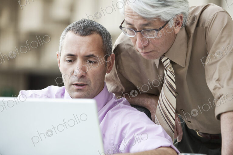An Asian businessman and Caucasian businessman working on laptop computer