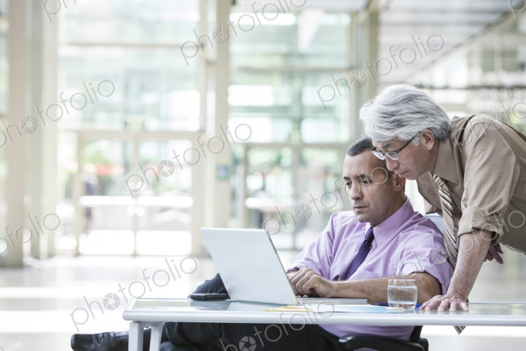 An Asian businessman and Caucasian businessman working on laptop computer