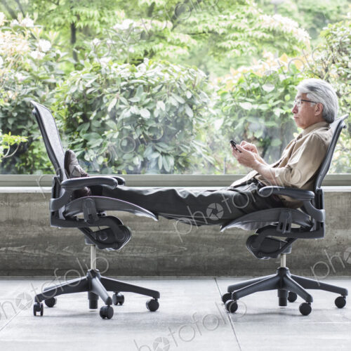 An Asian businessman checking his phone, sitting in a chair and resting his feet in… An Asian businessman checking his phone, sitting in a chair and resting his feet in…