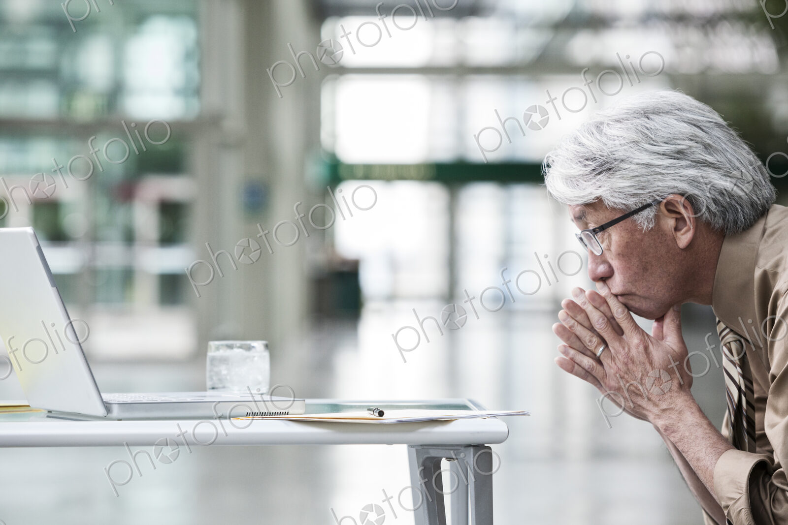 An Asian businessman ponders a problem on his laptop computer at his desk.