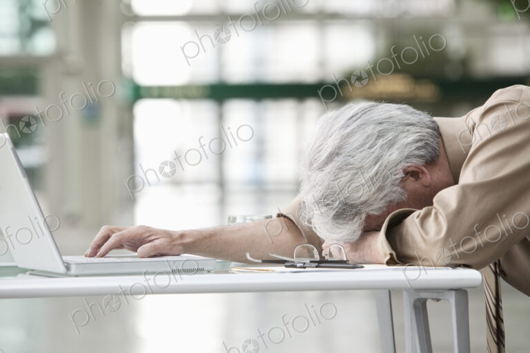 An Asian businessman ponders a problem on his laptop computer at his desk.