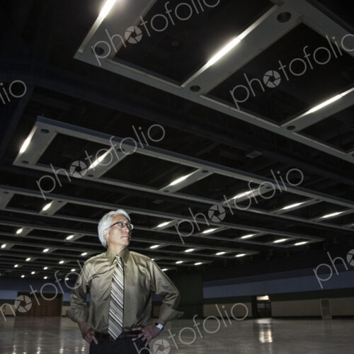 An Asian businessman standing in a dimly lit and dark exhibition area in a convention… An Asian businessman standing in a dimly lit and dark exhibition area in a convention…