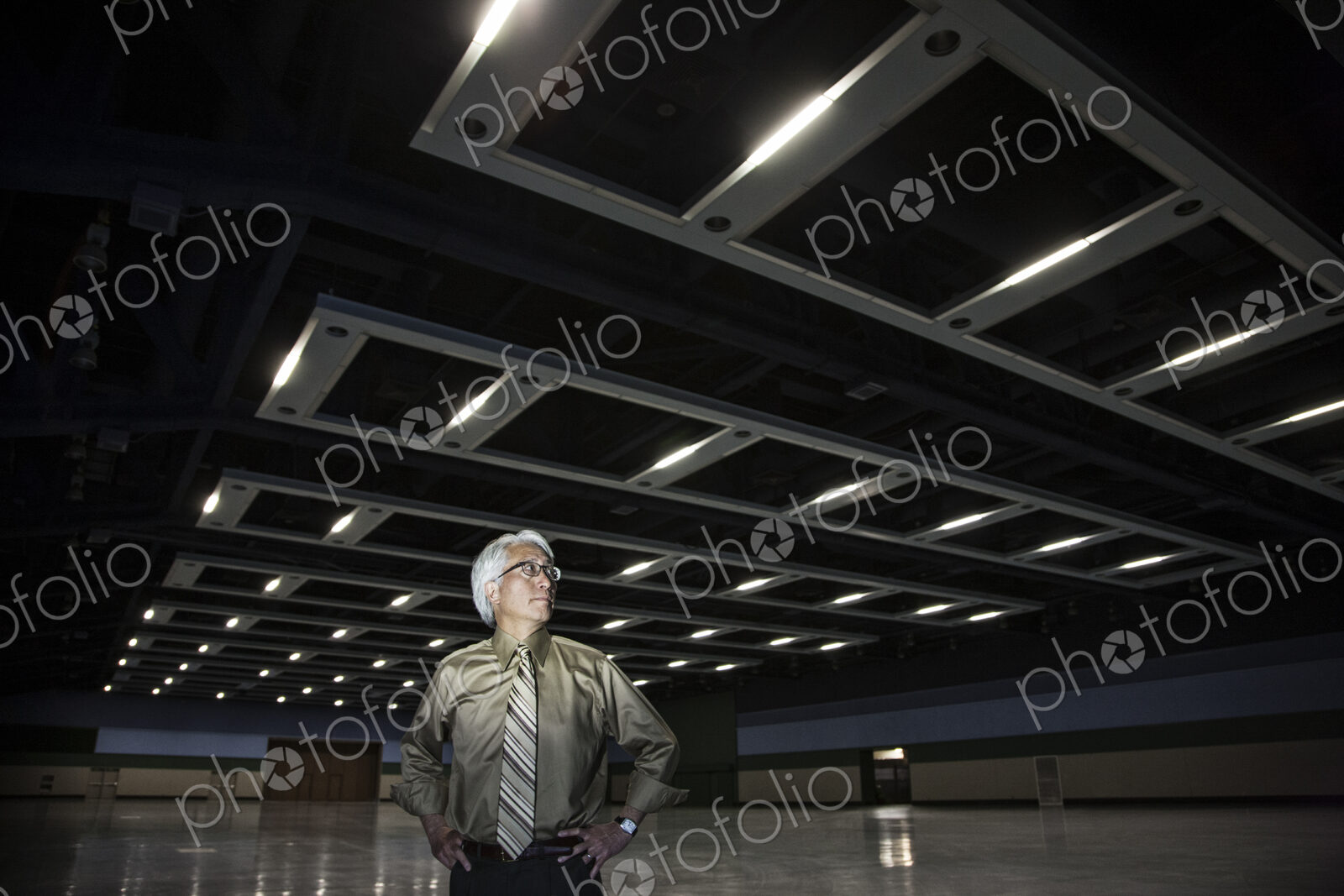 An Asian businessman standing in a dimly lit and dark exhibition area in a convention…