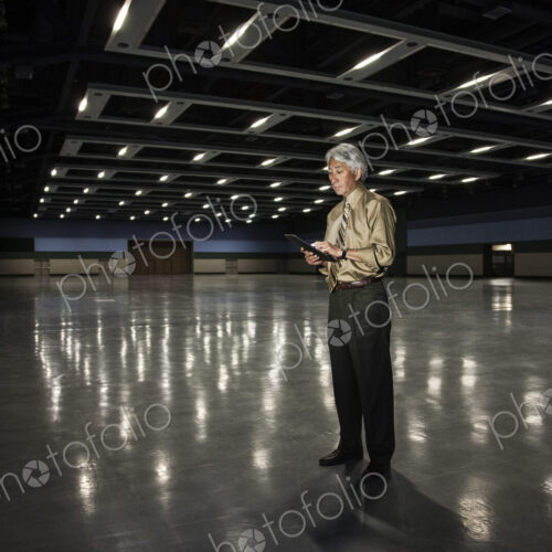 An Asian businessman standing in a dimly lit and dark exhibition area in a convention… An Asian businessman standing in a dimly lit and dark exhibition area in a convention…