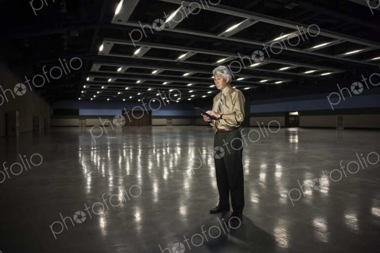 An Asian businessman standing in a dimly lit and dark exhibition area in a convention…
