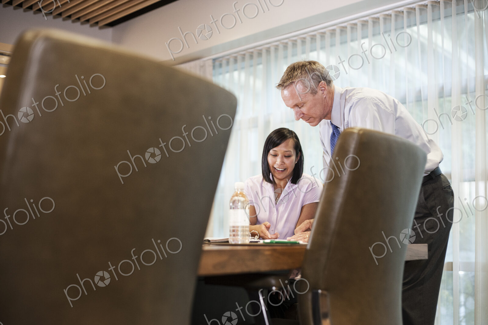 An Asian businesswoman and a caucasian businessman at work at a conference table.