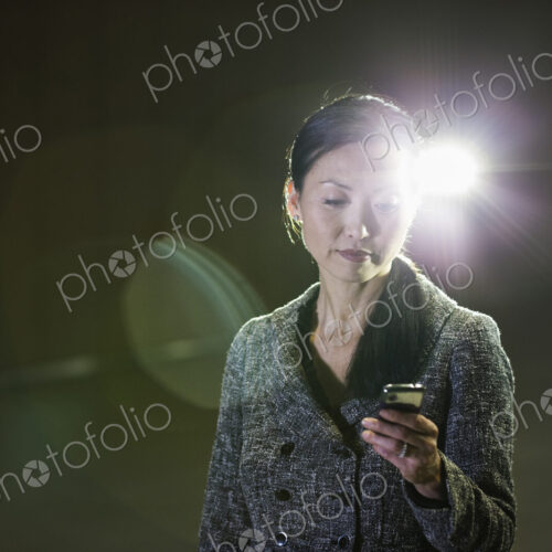 An Asian businesswoman in a spotlight working with her cell phone. An Asian businesswoman in a spotlight working with her cell phone.