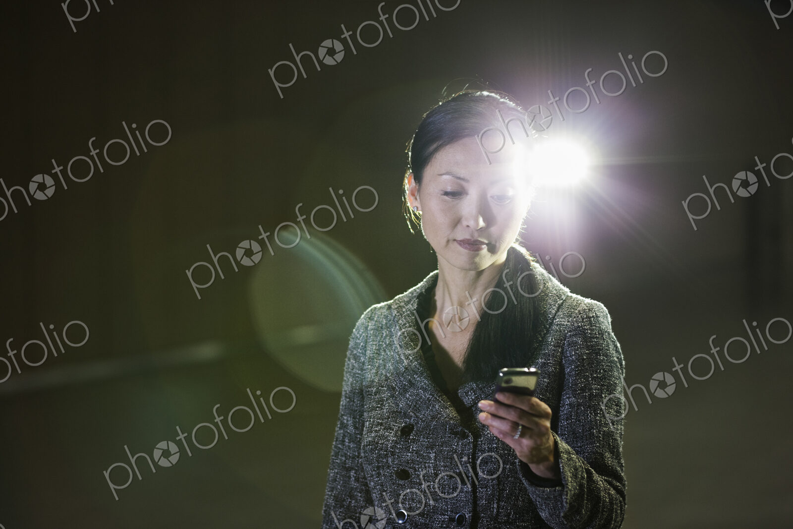 An Asian businesswoman in a spotlight working with her cell phone.