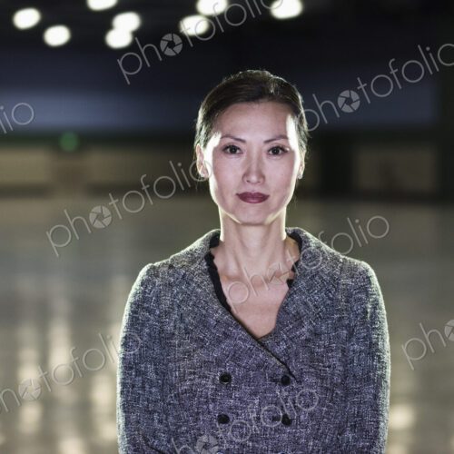 An Asian businesswoman standing in a dimly lit and dark exhibition area in a… An Asian businesswoman standing in a dimly lit and dark exhibition area in a…