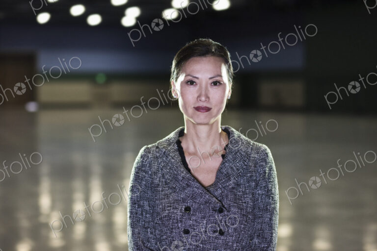 An Asian businesswoman standing in a dimly lit and dark exhibition area in a…
