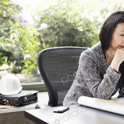 An Asian businesswoman working on architectural plans in her busiess office. An Asian businesswoman working on architectural plans in her busiess office.