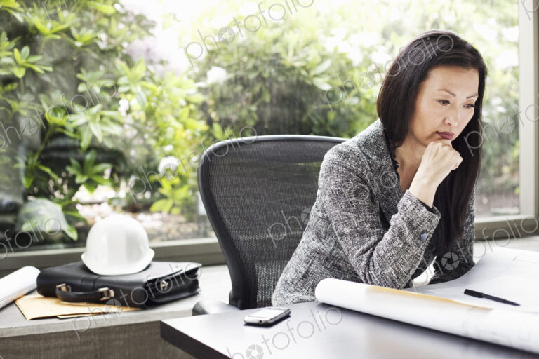 An Asian businesswoman working on architectural plans in her busiess office.