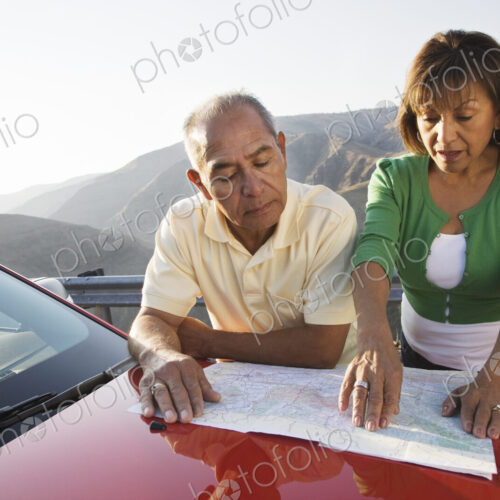 An Hispanic senior couple checking a paper map while pulled over at rest stop on a…