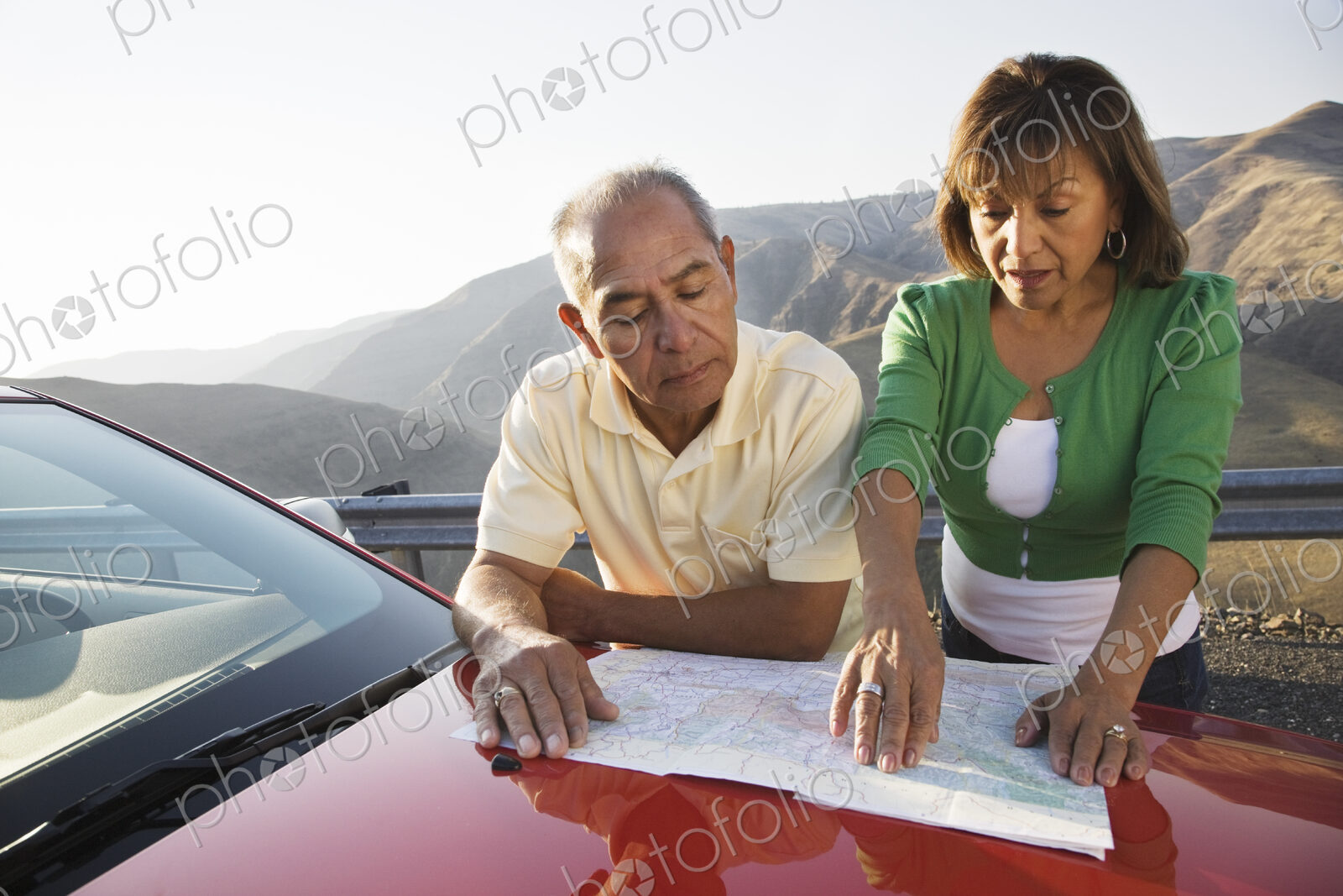 An Hispanic senior couple checking a paper map while pulled over at rest stop on a…