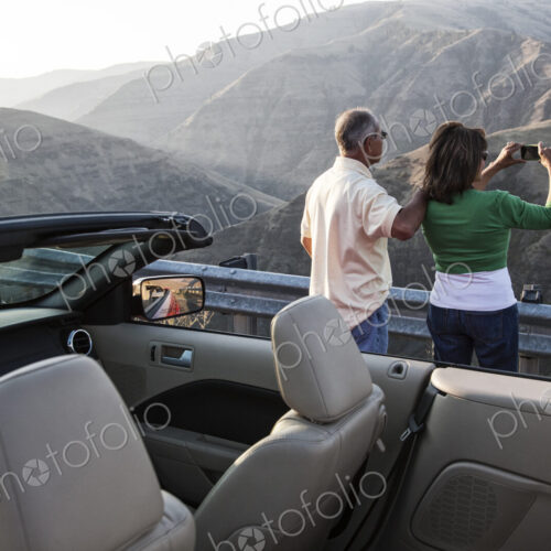 An Hispanic senior couple taking a picture of the scenery from a highway stop