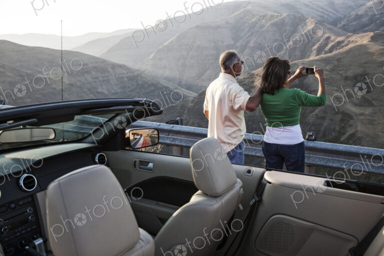 An Hispanic senior couple taking a picture of the scenery from a highway stop
