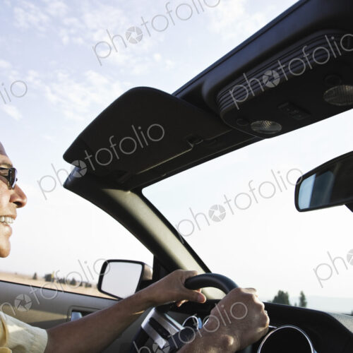 An Hispanic senior man laughing and driving his convertible sports car.