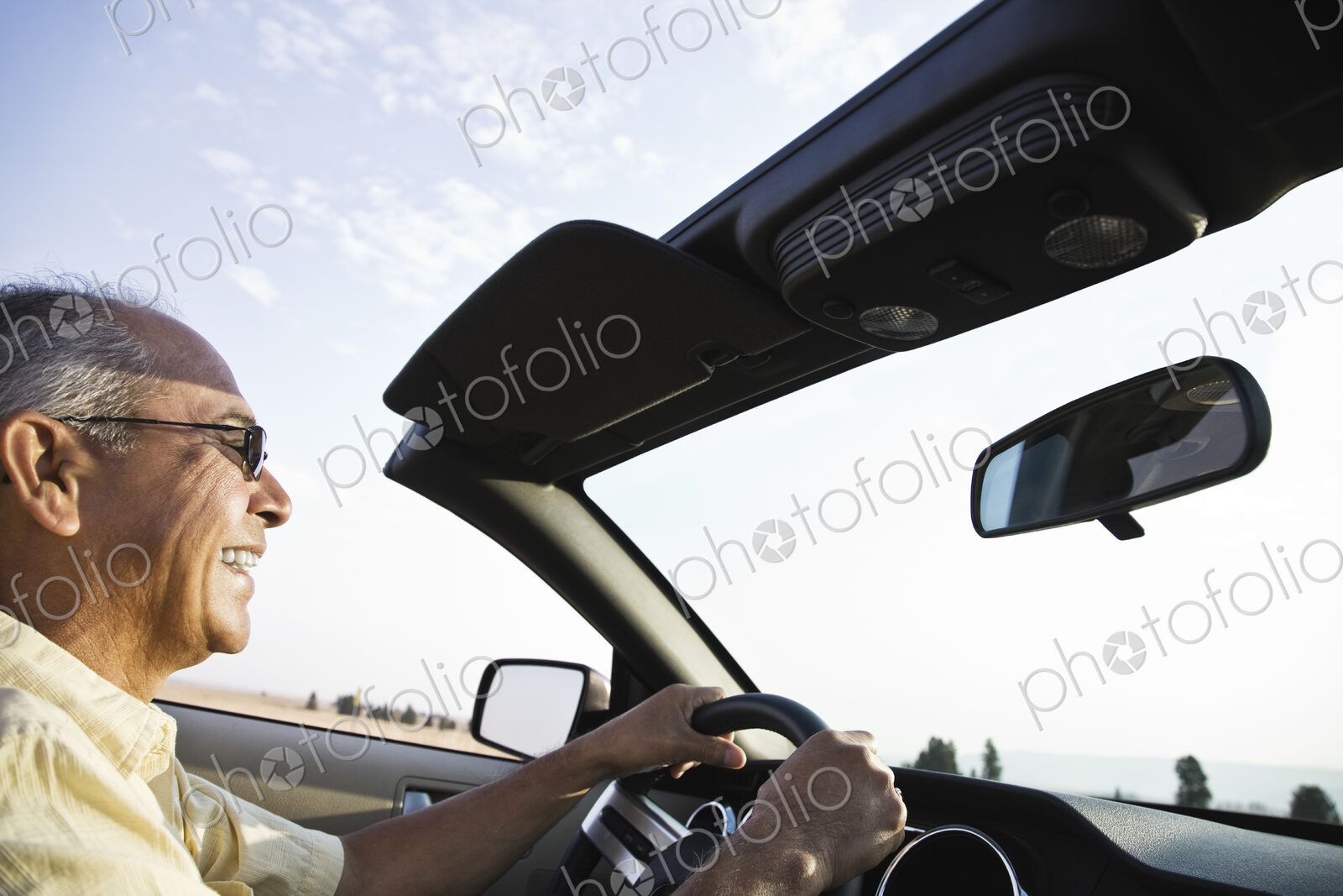 An Hispanic senior man laughing and driving his convertible sports car.