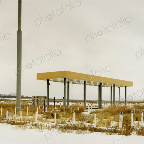 An abamdoned gas station, petrol station in the middle of nowhere, plants growing over…