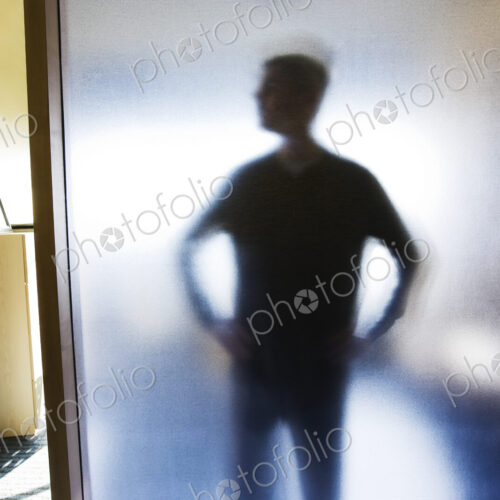 An abstract silhouette of a businessman distorted through a glass wall in an office. An abstract silhouette of a businessman distorted through a glass wall in an office.