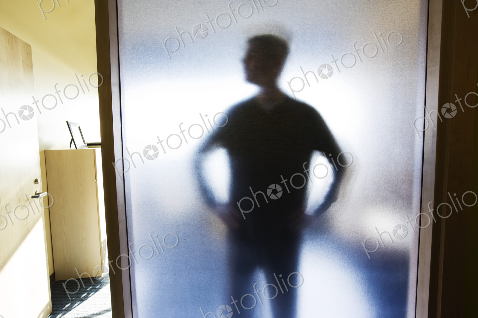 An abstract silhouette of a businessman distorted through a glass wall in an office.