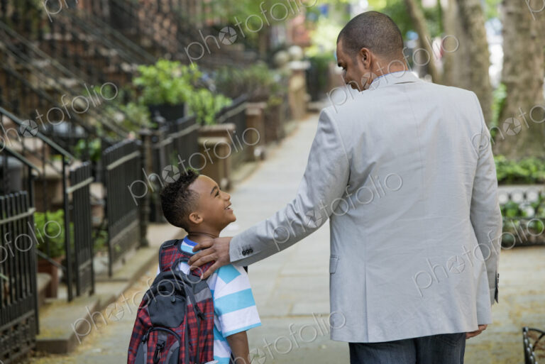 An adult and a child, a father and son, walking together on the street in the city.