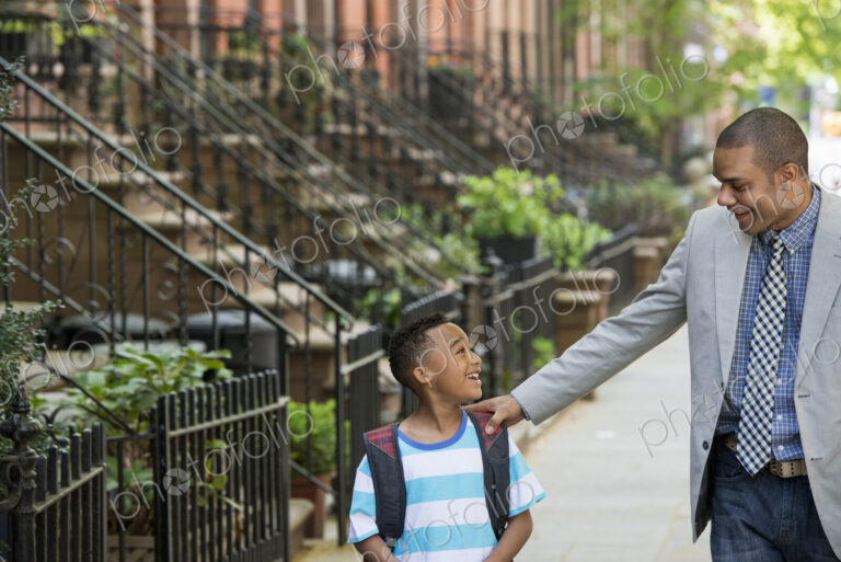 An adult and a child, a father and son, walking together on the street in the city.