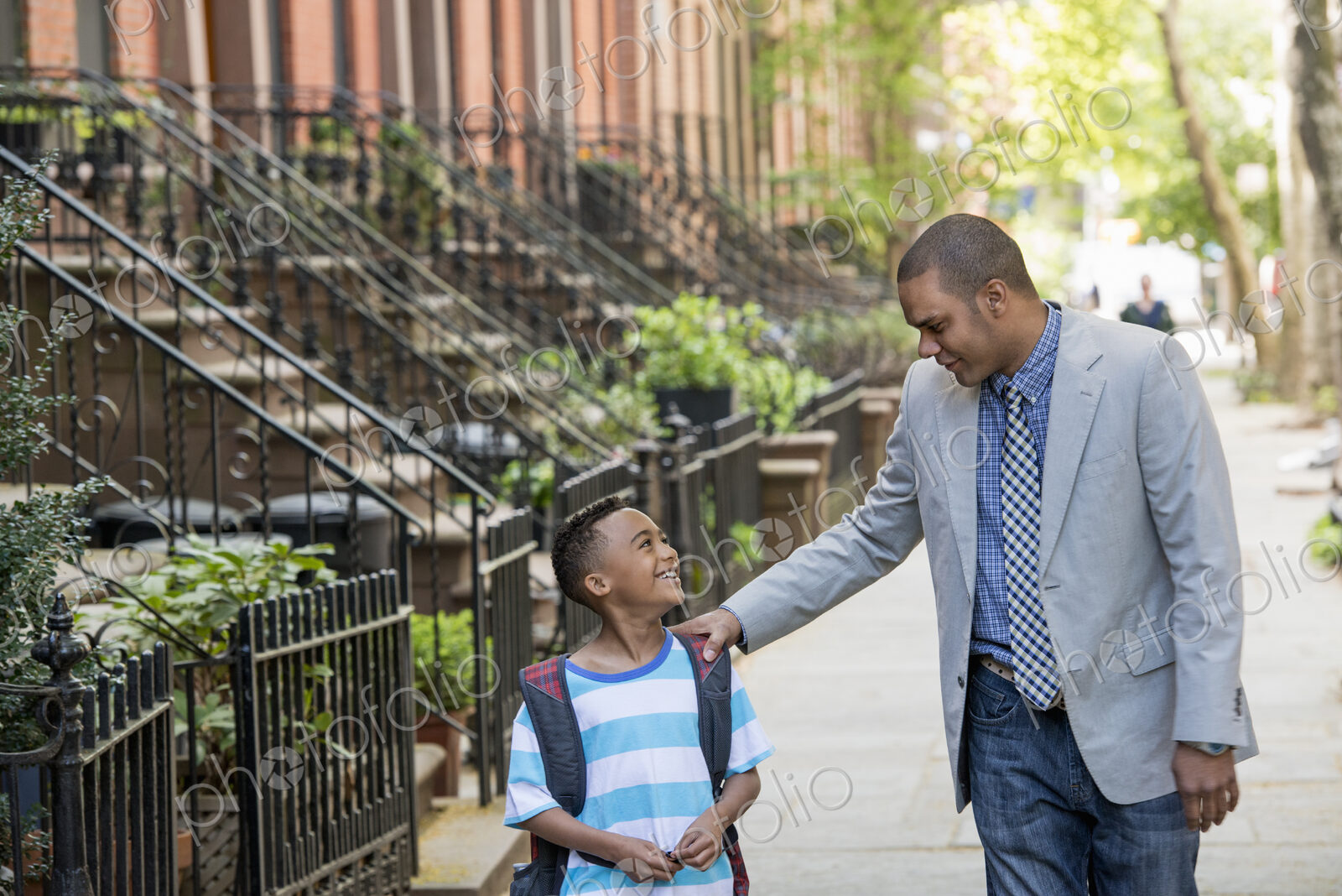 An adult and a child, a father and son, walking together on the street in the city.