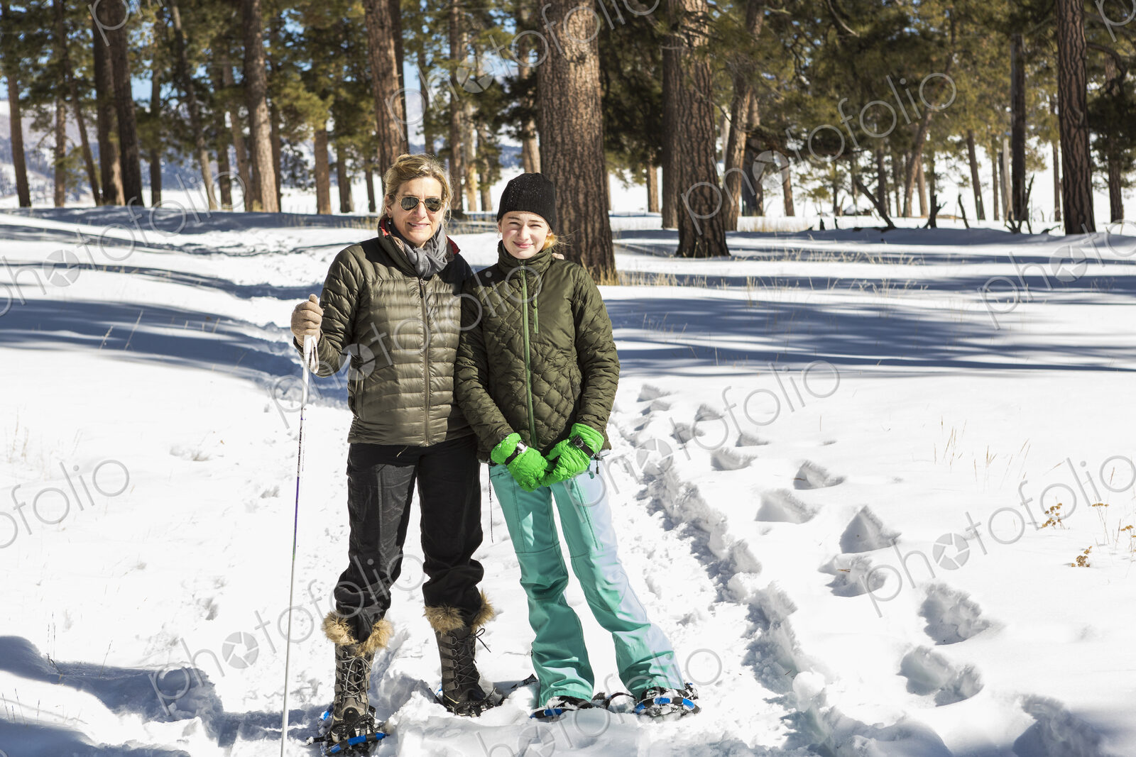 An adult woman and teenage girl in snow shoes in woodland holding ski poles