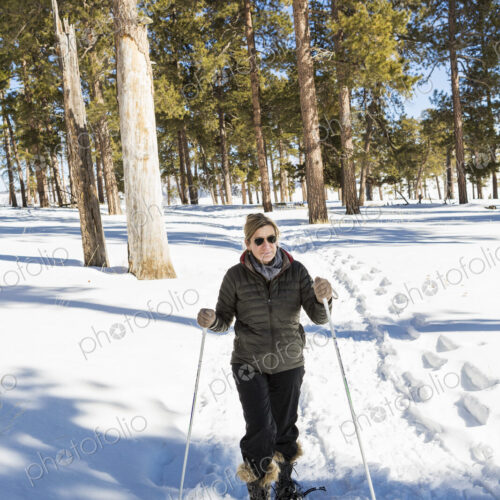 An adult woman in snow shoes in woodland holding ski poles