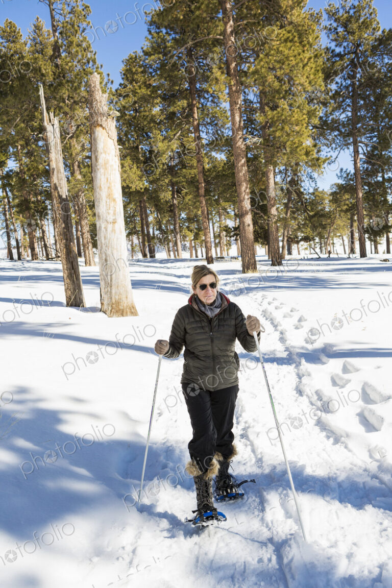 An adult woman in snow shoes in woodland holding ski poles