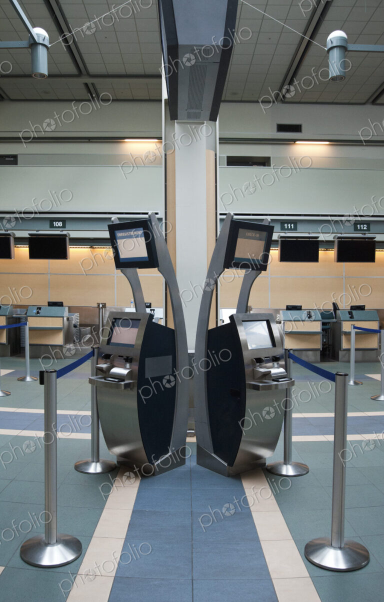 An airport check in area, closed desk and self check in terminals.