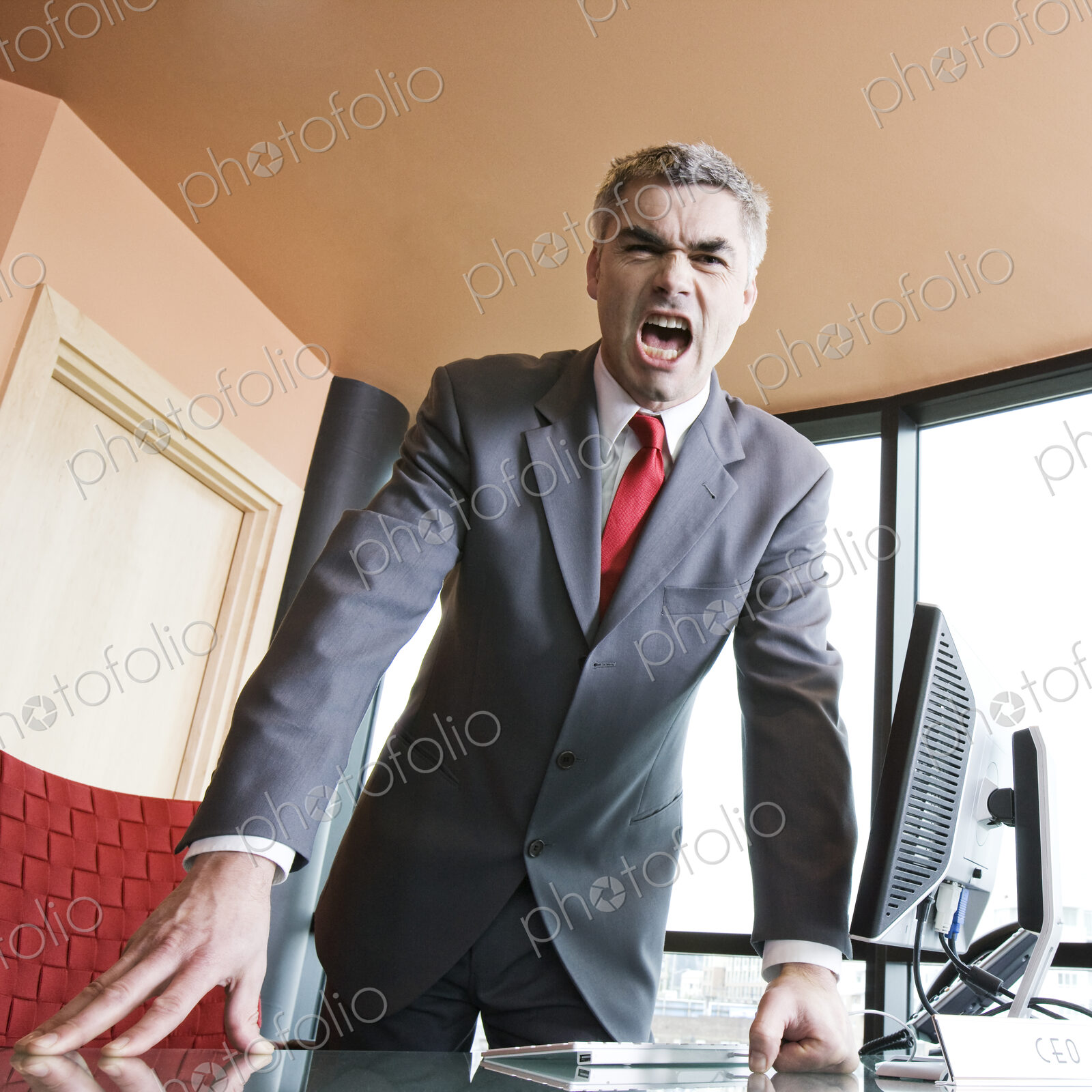 An angry caucasian businessman in a suit and tie yelling at the viewer of the photograph.