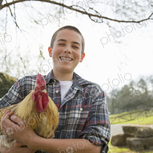 An animal sanctuary. A young boy holding a chicken with brown feathers and a red coxcomb. An animal sanctuary. A young boy holding a chicken with brown feathers and a red coxcomb.