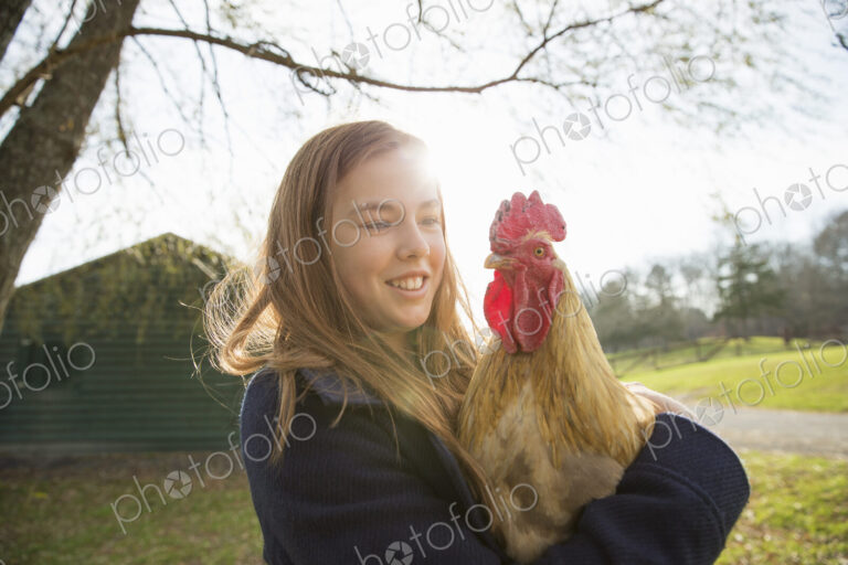 An animal sanctuary. A young girl holding a chicken with brown feathers and a red coxcomb.