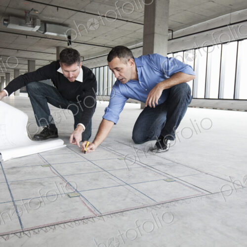 An architect and a business owner crouching over architectural plans planning new offices An architect and a business owner crouching over architectural plans planning new offices