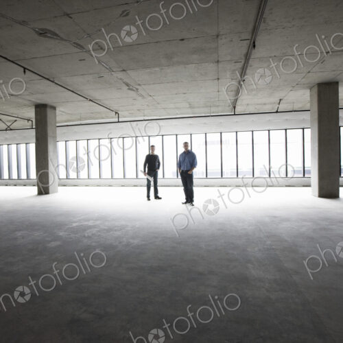 An architect and a business owner planning a new office space in an empty raw business…