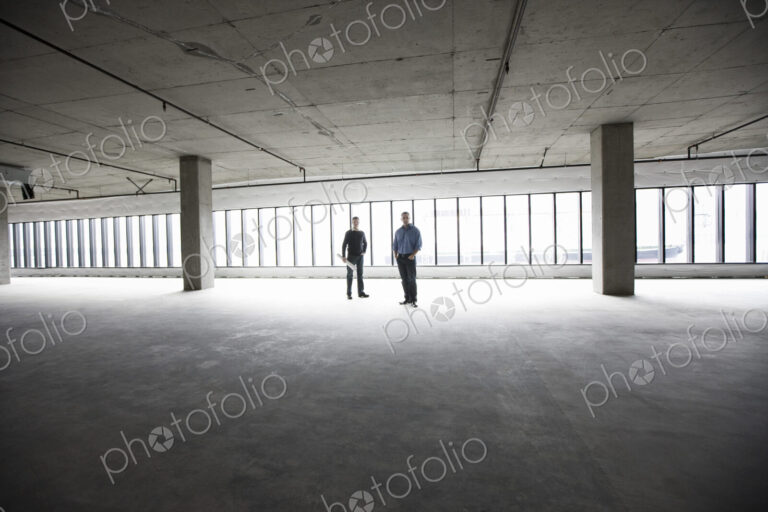 An architect and a business owner planning a new office space in an empty raw business…