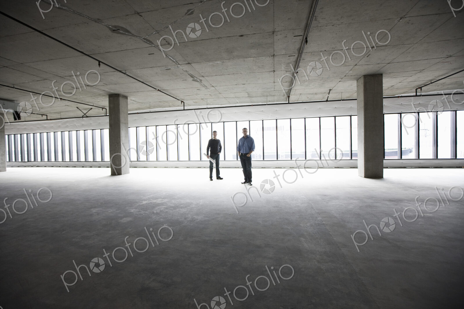 An architect and a business owner planning a new office space in an empty raw business…
